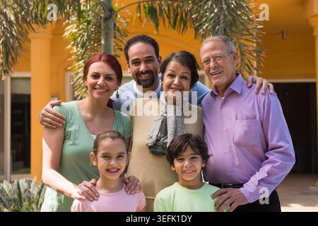 Moderne arabische Mehrgenerationsfamilie aus dem Nahen Osten, die vor ihrem Haus zusammen lächelt Stockfoto