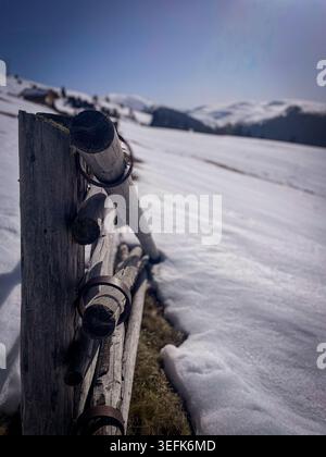 Rustikaler hölzerner Zaunpfosten, der in tiefem Schnee steht und die Grenze zu einem sonnigen Wintertag mit Bergkulisse markiert Stockfoto