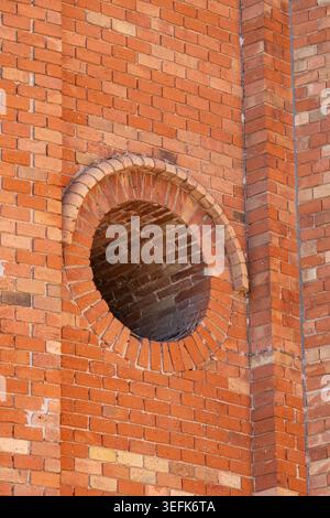 Nahaufnahme des Circular Brick Arch Fensters, das sich in der historischen roten Mauermauer öffnet Stockfoto