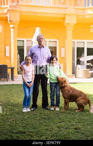 Moderner arabischer Großvater aus dem Nahen Osten mit Enkeln und Hund im Familiengarten bei sonnigem Haus Stockfoto