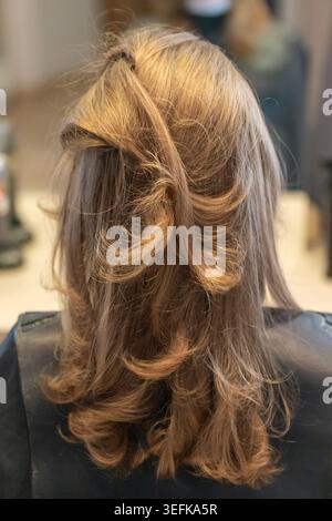 Rückansicht einer Frau mit gestyltem, welligem aschblondem Haar in einem professionellen Friseursalon. Stockfoto