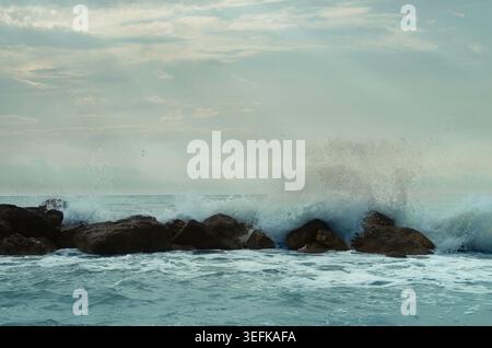 Stürmische Meereswellen stürzen gegen die Felsen, mit weißem Sprühnebel und dramatischer Meeresbewegung. Stockfoto
