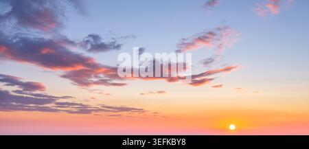Ein atemberaubender Sonnenuntergang färbt den Himmel in warmen Farbtönen, mit dramatischen Wolken, die eine wunderschöne Kulisse bilden, wenn die Sonne untergeht. Stockfoto