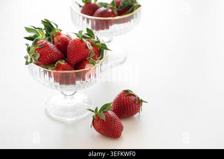 Elegante Komposition mit frischen roten Erdbeeren in dekorativen Glasschalen mit goldenen Rändern auf weißem Hintergrund Stockfoto