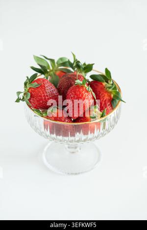 Elegante Komposition mit frischen roten Erdbeeren in dekorativen Glasschalen mit goldenen Rändern auf weißem Hintergrund Stockfoto