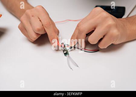 Elektrofachhände halten Multimeter-Tastköpfe, berühren kleine elektronische Leiterplatten auf weißer Oberfläche und führen elektrische Messungen durch Stockfoto