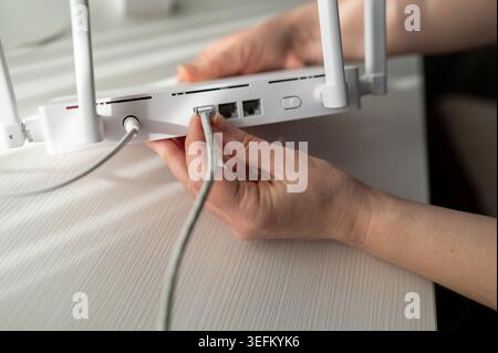 Nahaufnahme einer Person, die ein ethernet-rj45-Kabel und ein Netzteil an einen Wireless-Router mit Antennen angeschlossen hat. Konzept der Internet-Installation, Tech Stockfoto