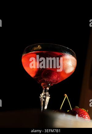 Roter Cocktail mit frischen Kirschen und Eiswürfeln, der ein erfrischendes alkoholisches Getränk in elegantem Coupé-Glas schafft, das Feierlichkeiten, Genießen und Verwöhnung betont Stockfoto