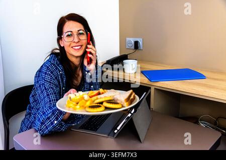 Frau, die während des morgendlichen Routinefrühstücks aus der Ferne arbeitet Stockfoto