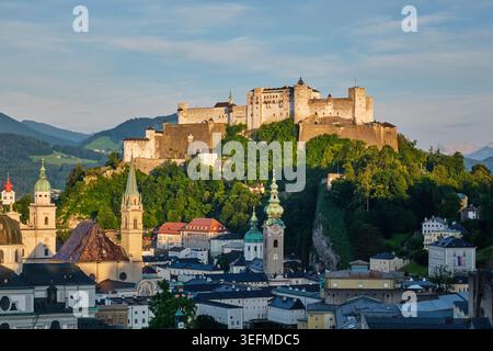 Nahaufnahme der mittelalterlichen Festung Hohensalzburg und der Kirchtürme in Salzburg, Österreich, in der Abenddämmerung. Stockfoto