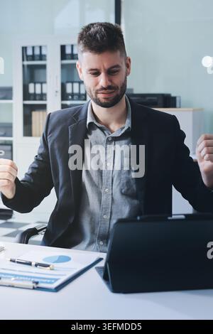 Der lächelnde Geschäftsmann im Anzug arbeitet in einem hellen, modernen Büro mit seinem Laptop Stockfoto
