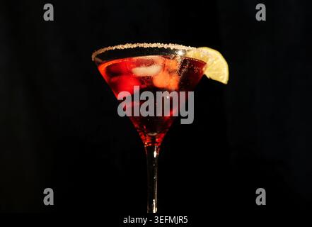 Roter Cocktail mit Eis und Orangenschale sitzt in einem Martiniglas mit Zuckerrand und schafft eine erfrischende und elegante Getränkeszene für einen Abend Stockfoto