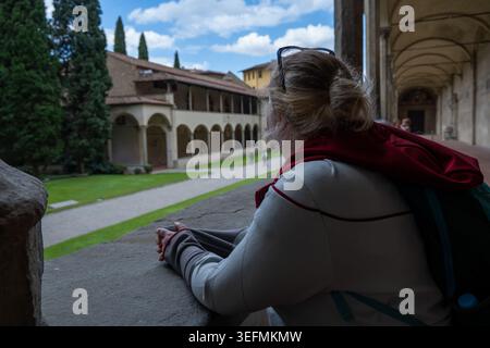 Reisende lehnen sich auf ein Steingeländer und blicken auf den Innenhof des Kreuzgangs an der Basilika Santa Croce in Florenz, Toskana, Italien, mit Bögen und Stockfoto