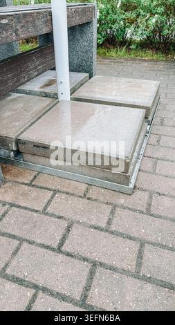 Nasse Betonplatten, die auf einer Metallpalette neben moderner Gartenanlage gestapelt sind. Industrielle Baumaterialien, die bei regnerischem Wetter erfasst wurden, ID Stockfoto