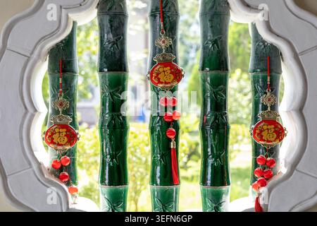 Grün glasierte Keramik-Bambusskulpturen mit roten chinesischen Glücksanhängern und Quasten füllen einen weißen bogenförmigen Fensterrahmen im Kek Lok Si Tempel in Penang, Malaysia. Der lebhafte Kontrast von Grün, Rot und weiß spiegelt die traditionelle chinesische dekorative Kultur wider. Stockfoto