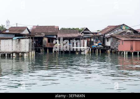 Traditionelle Holzpfahlhäuser eines Penang-Clan-Stegs erstrecken sich an einem bewölkten Tag über das ruhige Meer. Die verwitterten Strukturen spiegeln das lebendige Erbe dieser jahrhundertealten Fischergemeinden in George Town, Malaysia, wider. Stockfoto
