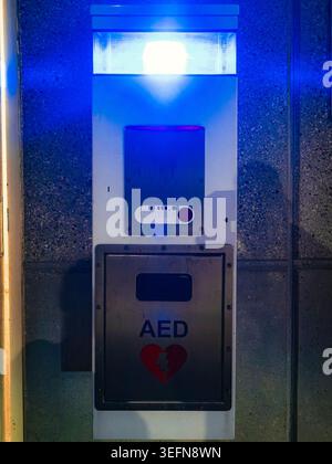 Automatisiertes externes Defibrillatorgerät und eine Notrufzentrale mit leuchtendem blauem Licht auf einer Wandplatte aus strukturiertem Stein Stockfoto