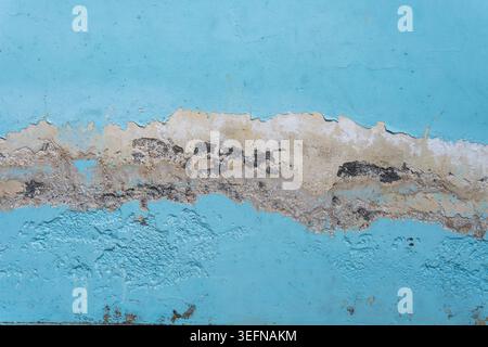 Eine Nahaufnahme eines Hintergrunds mit verwitterter hellblauer Farbe, die sich ablöst und rissig ist, um eine beschädigte Betontextur auf einer alten Wand freizulegen. Stockfoto