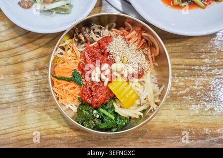 Erkunden Sie das lebendige Jeonju Bibimbap in Messing-, Stein- und Stahlschalen. Jedes Gericht wird mit frischem Gemüse, Rindfleisch und scharfem Gochujang garniert. Stockfoto