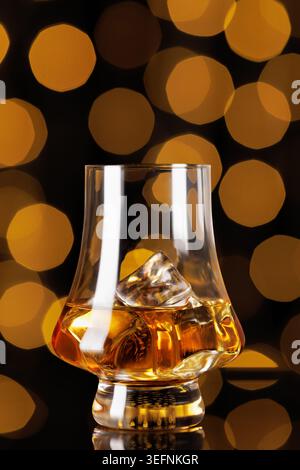 Bernsteinfarbener Whiskey mit schmelzenden Eiswürfeln in einem klaren Glas, der einen satten goldenen Farbton vor warmer, verschwommener Bokeh-Kulisse schafft Stockfoto