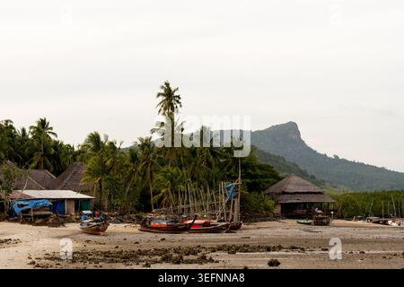 Krabi Thailand 19. Februar 2026 Strandhütten und Longtail-Boote säumen die Küste bei Ebbe in der Nähe von Palmen und Hügeln in Khlong Muang Stockfoto