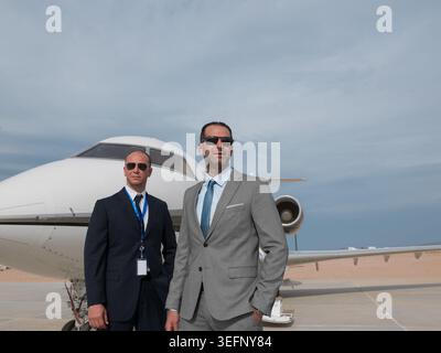 Geschäftsleute und Sicherheitsteam aus dem Nahen Osten stehen vor dem Privatjet auf dem Asphalt Stockfoto