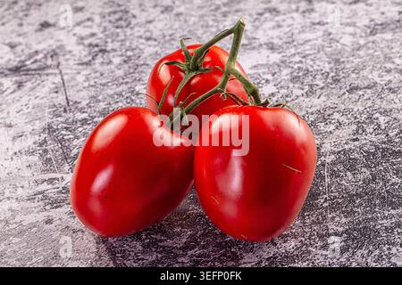 Eine lebhafte Gruppe von drei Reifen roten Tomaten auf einer grünen Rebe. Das frische Gemüse wird auf eine kontrastierende grauschwarze Oberfläche gestellt. Studio l Stockfoto