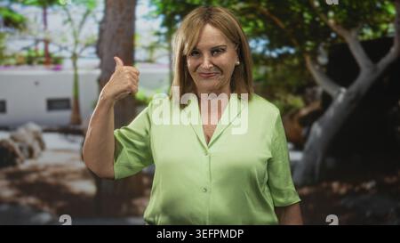 Eine ältere Frau von Middleage zeigt Daumen hoch mit Daumen und Hand und lächelt selbstbewusst vor einem Innenhof des Gebäudes; freundliche Zustimmung. Stockfoto