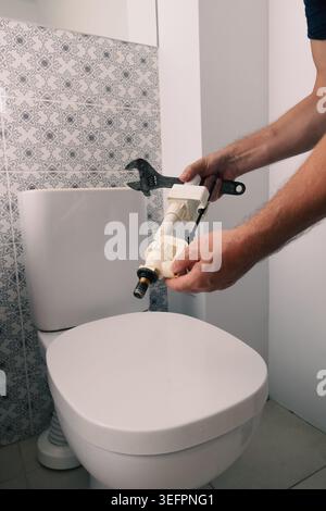 Nahaufnahme der Hände eines Handwerkers, der ein Ersatzventil für die Toilettenbefüllung und einen Schraubenschlüssel hält, während er an der Zisterne arbeitet. Hauswartung und Sanitär-Reparatur Stockfoto