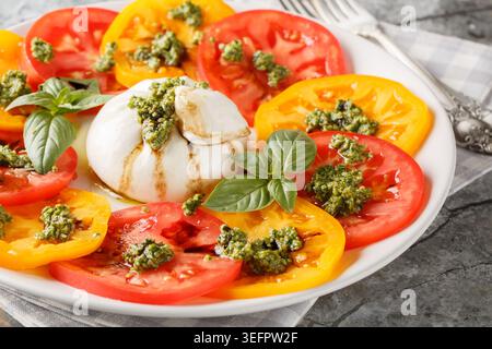 Caprese-Salat mit Burrata, Tomaten, Basilikum-Pesto und Balsamico-Essig in einem Teller auf dem Tisch. Horizontal Stockfoto