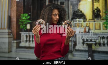 Frau, die zwei Schokoladenkrapfen in den Händen hält, während sie sie studiert; ruhige Besinnung. Stockfoto