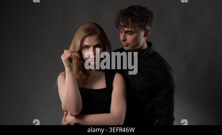 Junger Mann, der hinter der Frau steht und beide mit Intimität direkt in die Kamera blickt Stockfoto