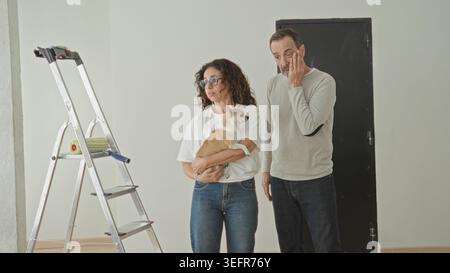 Frau, die einen kleinen Hund neben der Leiter hält, Hand an Stirn und Mann mit Hand an Hüfte im Gebäude; Sorge um Planungsentscheidung. Stockfoto