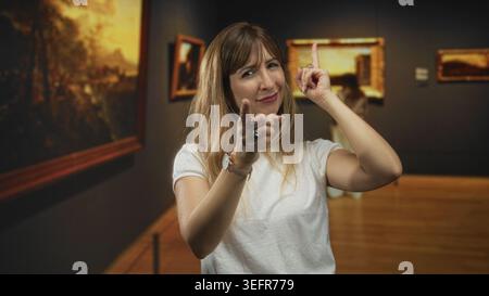 Die Frau zeigt den Finger nach vorne und zeigt die Punkte im Galeriebau nach oben, die Hände sind sichtbar und die Finger klingen; spielerische Neugier. Stockfoto