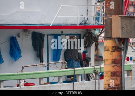 Yilan, Taiwan - 31. März 2025: Fisherman betritt eine Schiffskabine im Hafen von Nanfangao, mit Regenmänteln und Arbeitskleidung, die an der Außenseite des Bootes hängen. Stockfoto