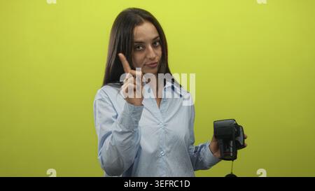 Frau in hellblauem Hemd, die Kamera mit dem Finger in der rechten Hand in einem hellgrünen Studio hält; ernste Warnung. Stockfoto