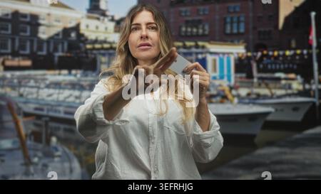 Frau, die eine Kreditkarte hält und mit dem Finger nach vorne zeigt, mit Booten am Hafen; Selbstvertrauen stärken. Stockfoto