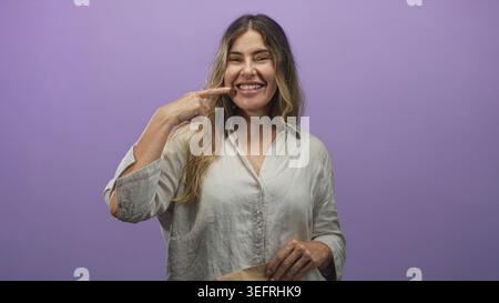 Frau zeigt mit dem Finger auf die Papiertüte im Studio, während sie lächelt, Mund und Zähne sichtbar; fröhliche Enthüllung. Stockfoto