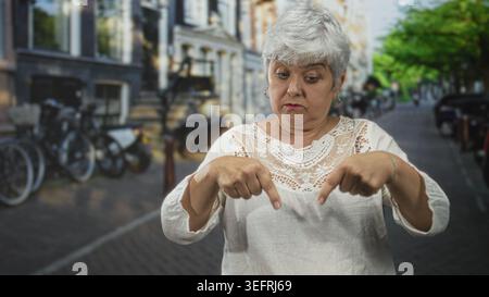 Die Frau zeigt mit beiden Zeigefingern auf den Bürgersteig einer Stadtstraße mit Fahrrädern. Sie sieht hart und hartnäckig aus; warnt frustrierend. Stockfoto