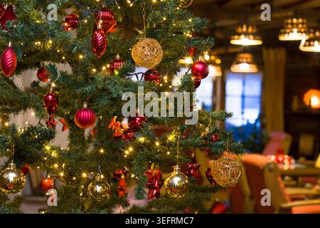Geschmückter Weihnachtsbaum mit leuchtenden Lichtern, goldenen und roten Kugeln aus nächster Nähe. Festliche Feiertage verwischte Zimmereinrichtung im Hintergrund, Tirol, Österreich Stockfoto
