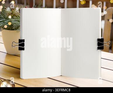 Öffnen Sie leeres Notizbuch Modell oben mit Binder Clips auf rustikalem hölzernem Hintergrund mit Weihnachtslichtern und festlichem Neujahrsbokeh. Vorlage für Feiertagswünsche Stockfoto