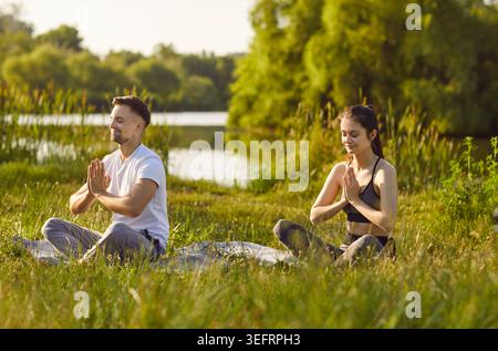 Entspannte junge Männer und Frauen, die in Lotuspositionen über die Natur meditieren und Yoga-Übungen im Freien genießen. Stockfoto