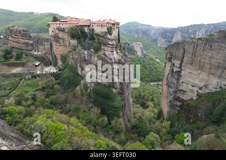 Ein beeindruckender Blick auf das Heilige Kloster von Varlaam, das auf einer massiven Felssäule sitzt, mit Blick auf die tiefgrünen Täler von Zentralgriechenland. Stockfoto