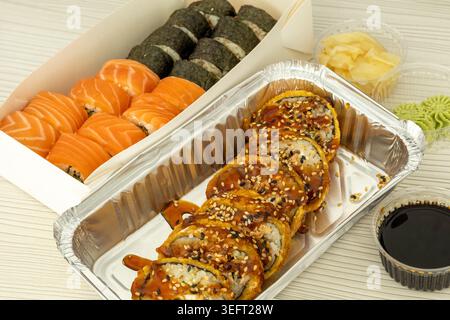 Verschiedene Sushi-Sets mit Lachsbrötchen, Meeresalgen-Maki, knusprigem gebratenem Sushi, Sojasauce, Wasabi und eingelegtem Ingwer in Take-Out-Behältern Stockfoto