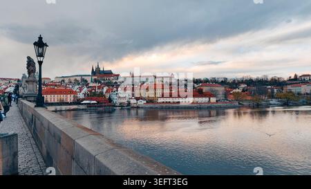 Blick auf die Stadt über den Fluss von der historischen Steinbrücke in der Abenddämmerung, alte europäische Gebäude und Kathedrale auf der Skyline, bewölkter Himmel reflektiert in ruhigem Wasser Stockfoto