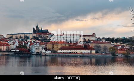 Wunderschöner Blick auf die Prager Burg und Hradcany von der Karlsbrücke. Historisches Stadtbild am Flussufer mit Gebäuden mit roten Dächern und Schloss auf einem Hügel unter Mo Stockfoto