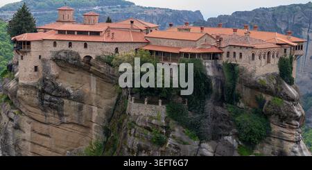Breiter Panoramablick auf das Kloster Varlaam, das auf einer massiven Klippe thront, mit seinem einzigartigen Steinmauerwerk und den rot gekachelten byzantinischen Dächern. Stockfoto