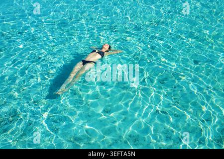 Frau im Bikini, die sich entspannt und auf dem Rücken in wunderschönem türkisfarbenem Wasser auf den Malediven schwimmt Stockfoto