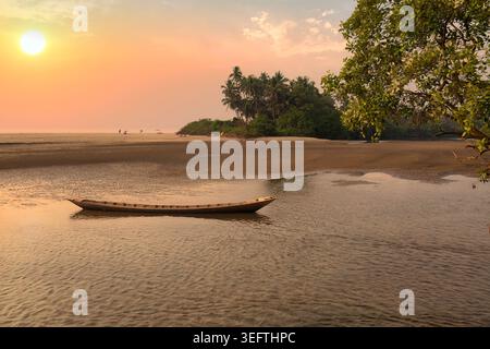 Pittoresker Sonnenuntergang mit Kanu und Palmen in der Nähe von Anjuna Beach im Norden Goas, Indien Stockfoto