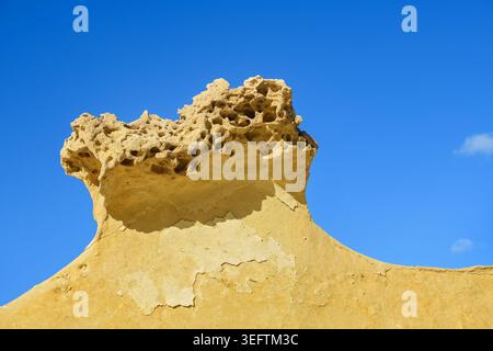 Nahaufnahme eines verwitterten gelben Kalksteinfelsens, der durch Erosion geformt wurde, mit markanten Löchern, die sich von einem leuchtenden, klaren blauen Himmel abheben. Stockfoto